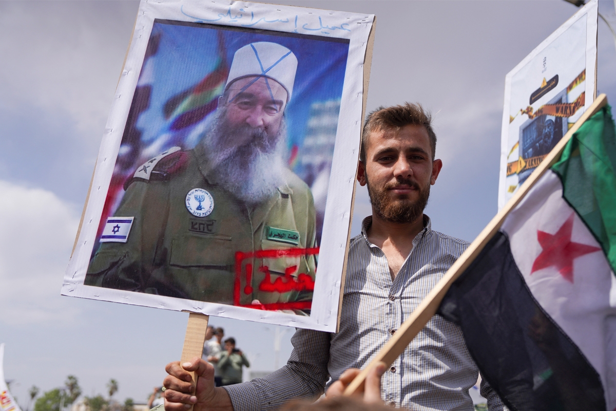 متظاهر يرفع صورة للهجري باللباس العسكري الإٍسرائيلي في حماة أمس (رويترز)