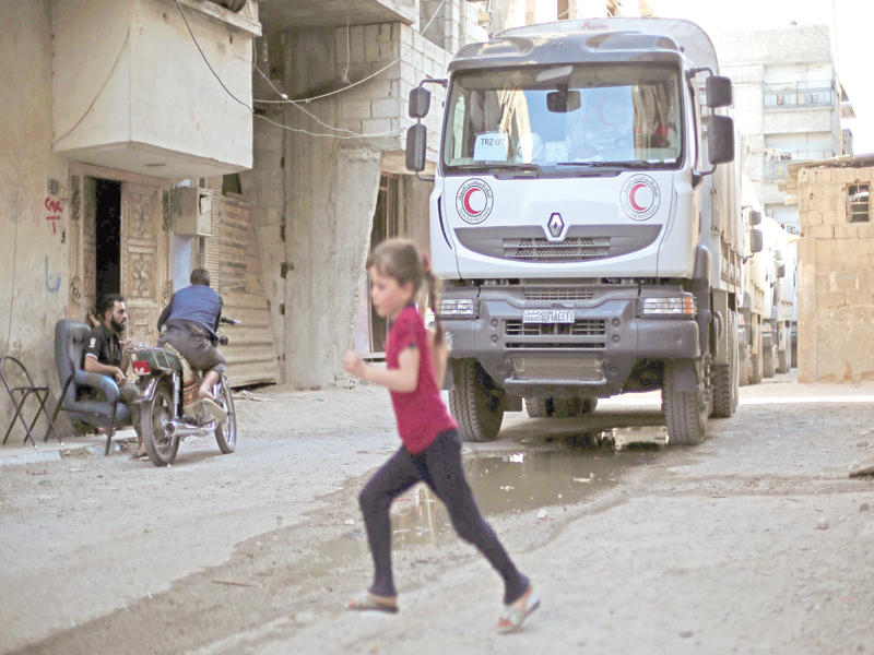 صبي سوري يمر أمام قافلة مساعدات لدى دخولها أمس الأول بلدة زملكا المحاصرة من قبل النظام للمرة الأولى منذ أربع سنوات (أ ف ب)