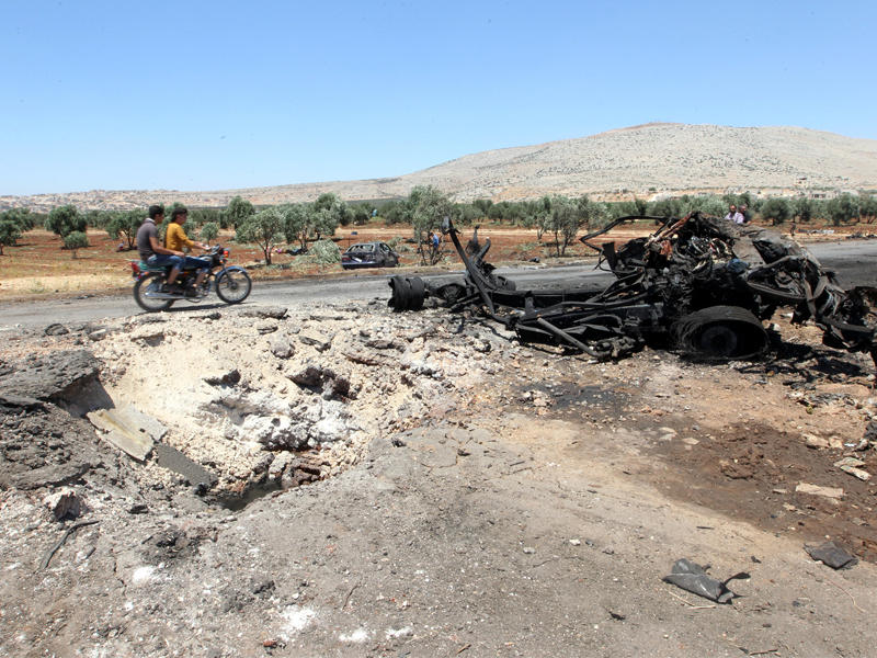 سوريان على دراجة نارية يتفقدان ناقلة وقود دمرتها غارة نظامية على طريق بلدة ترمانين في إدلب أمس الأول (رويترز)