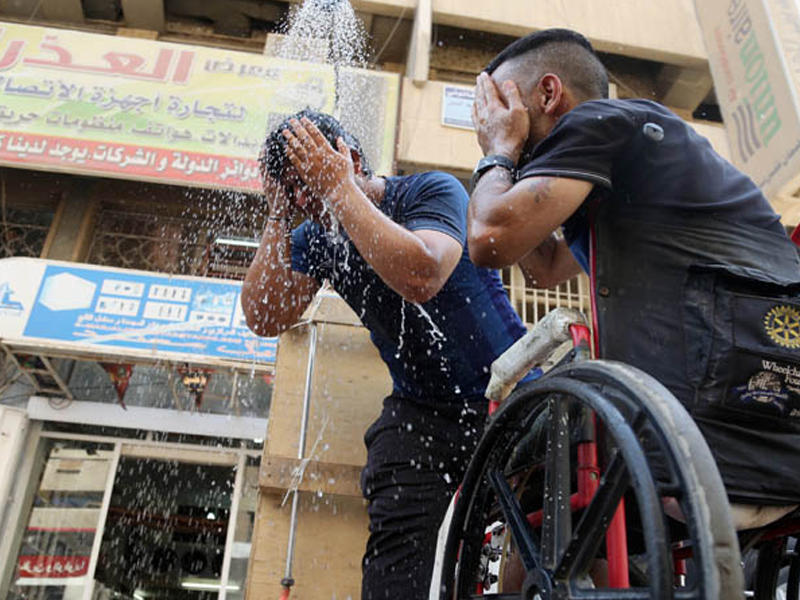 شابان عراقيان يرشان رأسيهما بالماء بحثاً عن قليل من البرودة في أجواء تجاوزت درجة حرارتها الخمسين مئوية