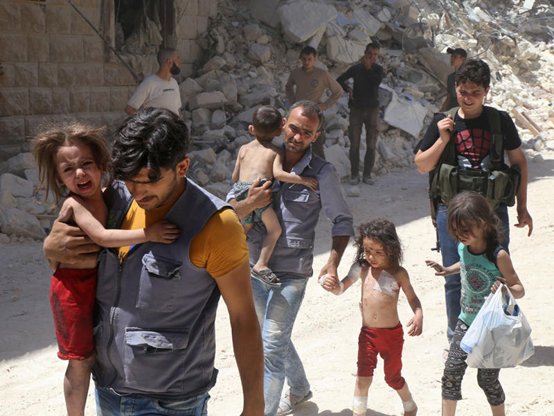 رجلان من أهالي مدينة حلب يحملان أطفالهما خارجين من المباني المدمرة بفعل القصف في منطقة المشهد شمال المدينة