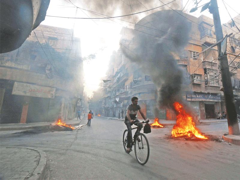 سوري على دراجة هوائية يمر بين إطارات أشعلها المقاتلون لتشويش رؤية الطائرات المحلقة فوق حلب (رويترز)