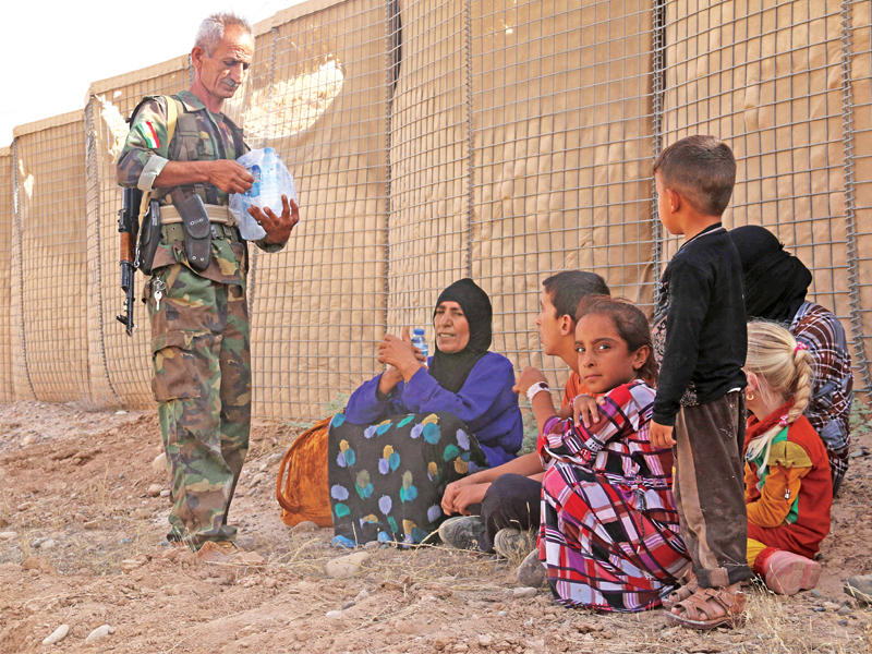 جندي يوزع الماء على الفارين من «داعش» في الحويجة أمس  (أ ف ب)