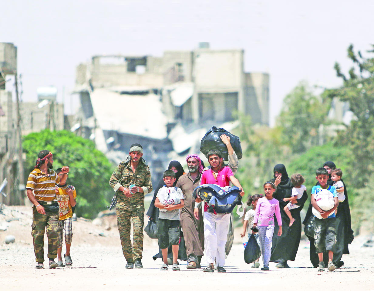 سوريون يعودون إلى منازلهم في منبج أمس الأول برفقة مقاتل من «قسد»   (رويترز)