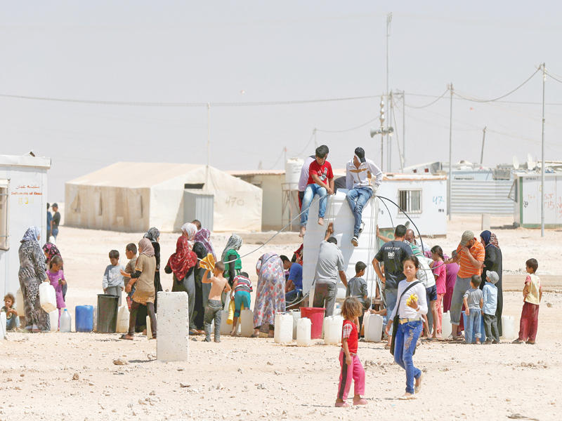 لاجئون سوريون يتجمعون حول خزان مياه في مخيم الزعتري بالأردن أمس (رويترز)