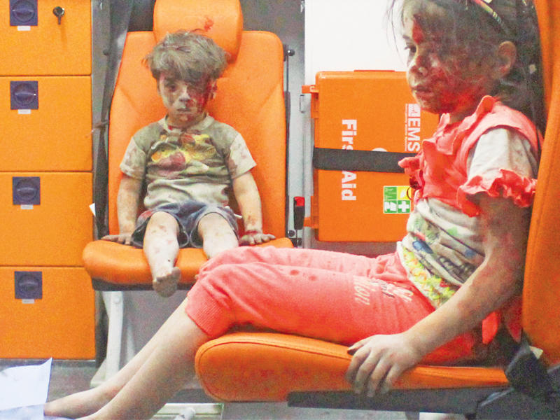 الطفل عمران دقنيش وأخته بانتظار العلاج في سيارة إسعاف بعد انتشالهما من تحت أنقاض منزلهما في حي القاطرجي شرق مدينة حلب أمس الأول (رويترز)n