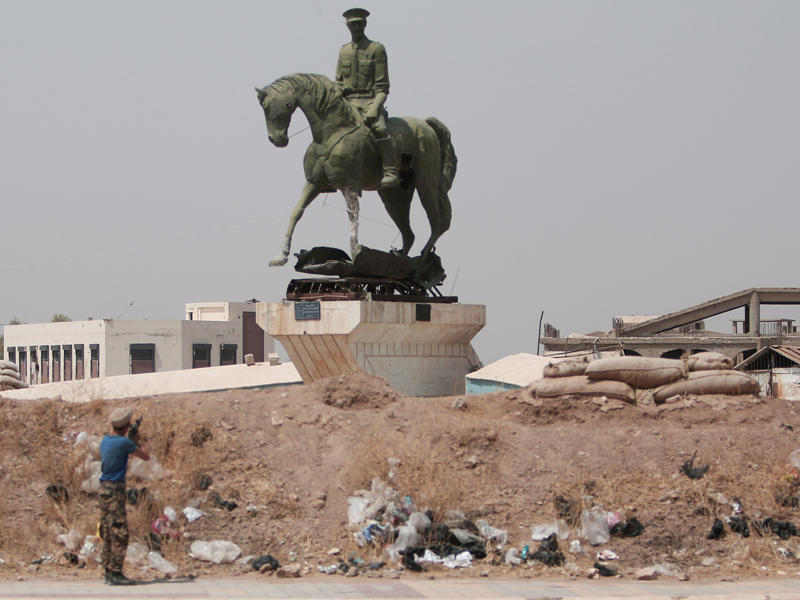 مقاتل كردي يرمي طلقات نارية تجاه نصب باسل الأسد
