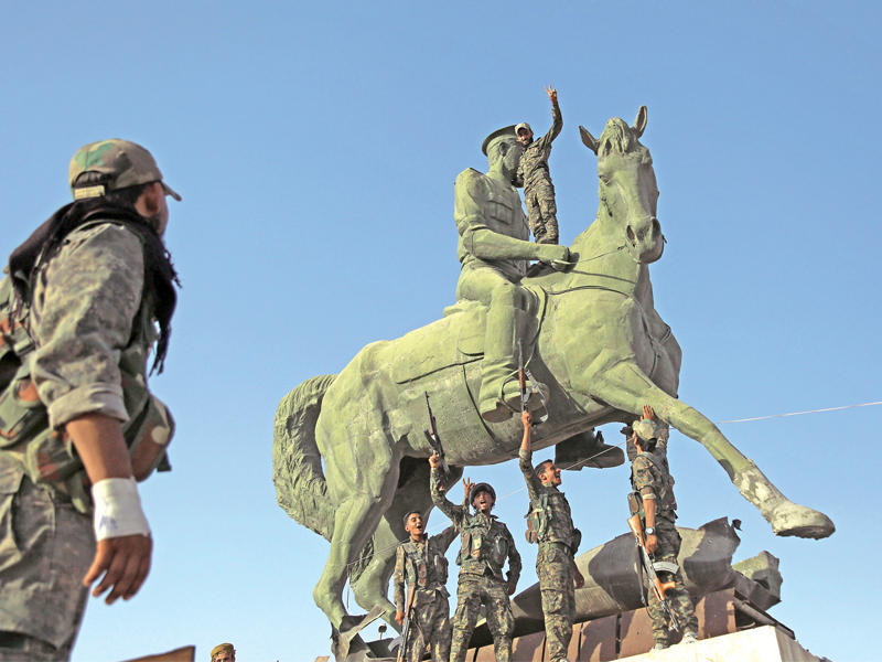 عناصر من «الأسايش» فوق تمثال باسل الأسد في الحسكة أمس الأول (أ ف ب)