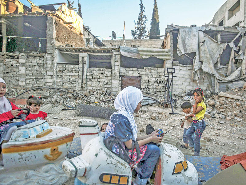 أطفال سوريون يلهون بين الدمار أمس الأول في ثاني أيام عيد الأضحى بمدينة دوما قرب دمشق (إي بي أيه)