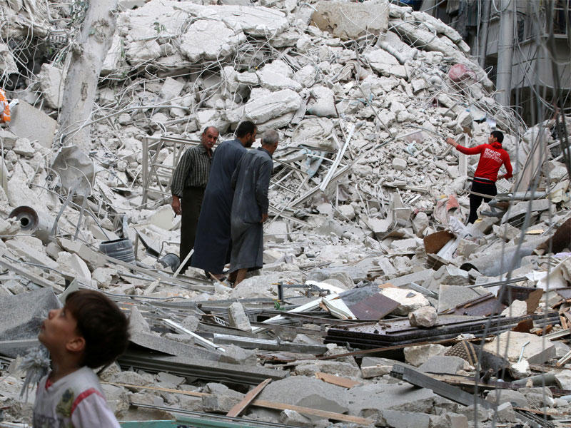 سوريون في موقع تعرض لغارات أمس في حي طريق الباب بحلب الشرقية                  (رويترز)