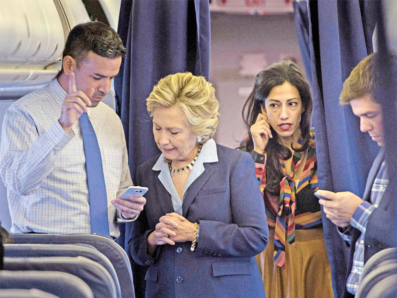 كلينتون تتفقد هاتف سكرتيرها الإعلامي بريان فالون وتبدو خلفها مساعدتها هوما عابدين في الطائرة إلى نيويورك أمس (أ ف ب) 