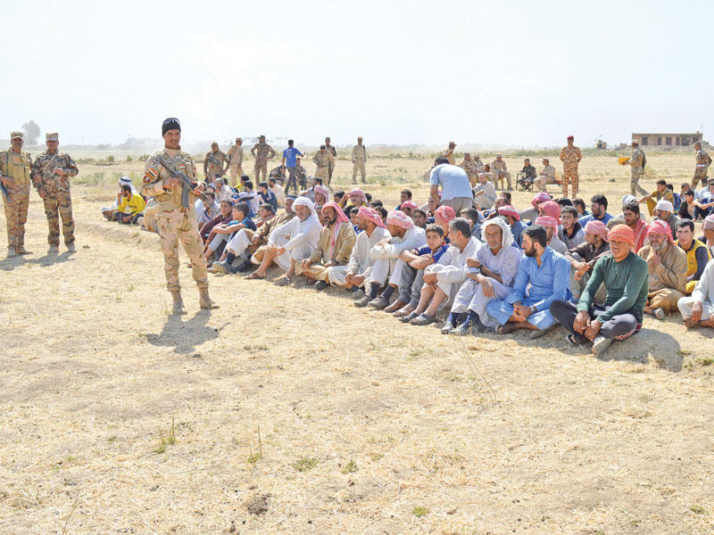 رجال عراقيون مهجرون من الرمادي ينتظرون الفحص الأمني للسماح لهم بالمغادرة أمس (رويترز)