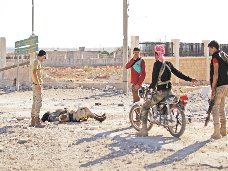 جثة داعشي تستوقف مقاتلين معارضين في قرية تركمان البارح شمال حلب أمس الأول  (رويترز)