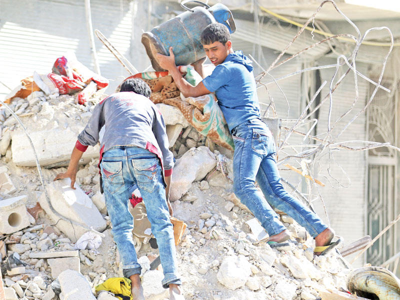 سوري يخرج بقنينة غاز من منزله المدمر في حي القاطرجي أمس (رويترز)