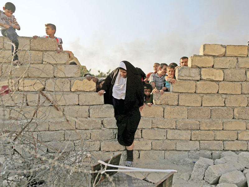 عراقية إلى جانبها مجموعة من الأطفال يتسلقون جداراً للوصول إلى مساعدات إنسانية في القيارة، جنوب الموصل أمس (رويترز)