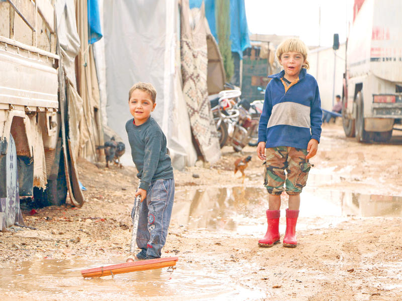 صبيان سوريان يدفعان ماء المطر عن خيمة ذويهما في مخيم باب سلامة خارج مدينة أعزاز على الحدود مع تركيا أمس الأول (أ ف ب)