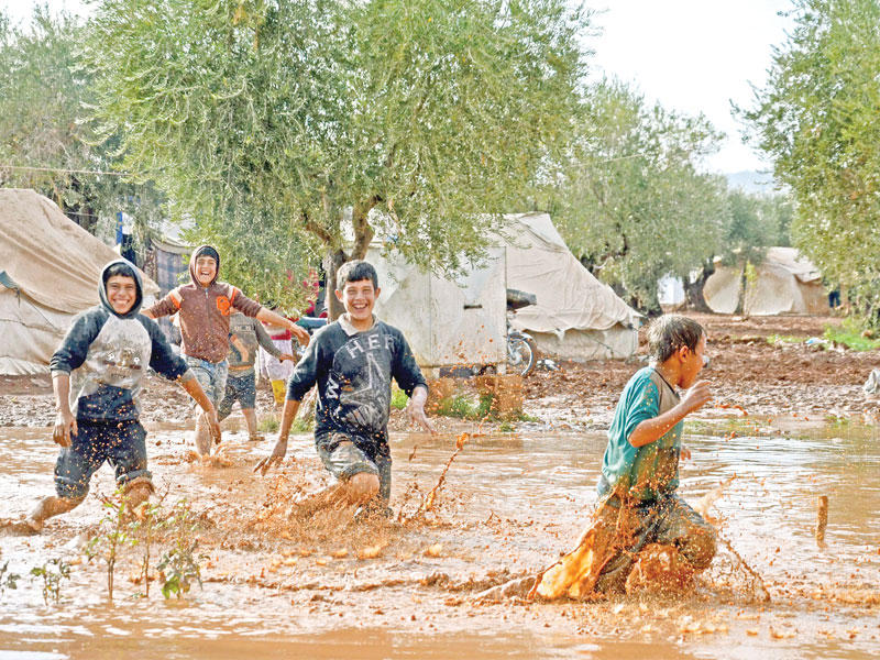 صبية يلعبون في بركة مطر في مخيم أعزاز على حدود تركيا أمس (أ ف ب)