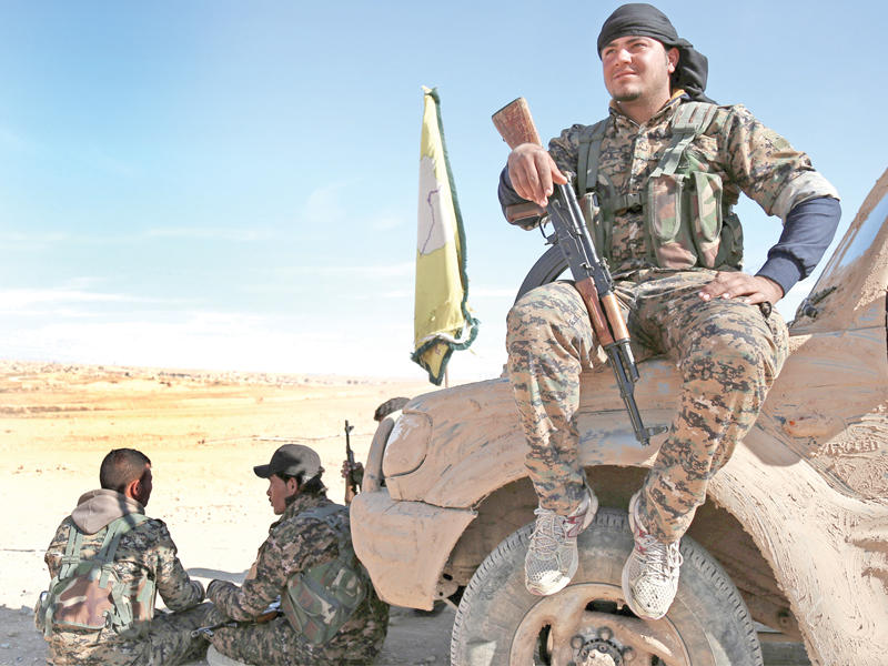 مقاتلون أكراد في استراحة على وأمام سيارة مموهة بالطين شمال الرقة (رويترز)