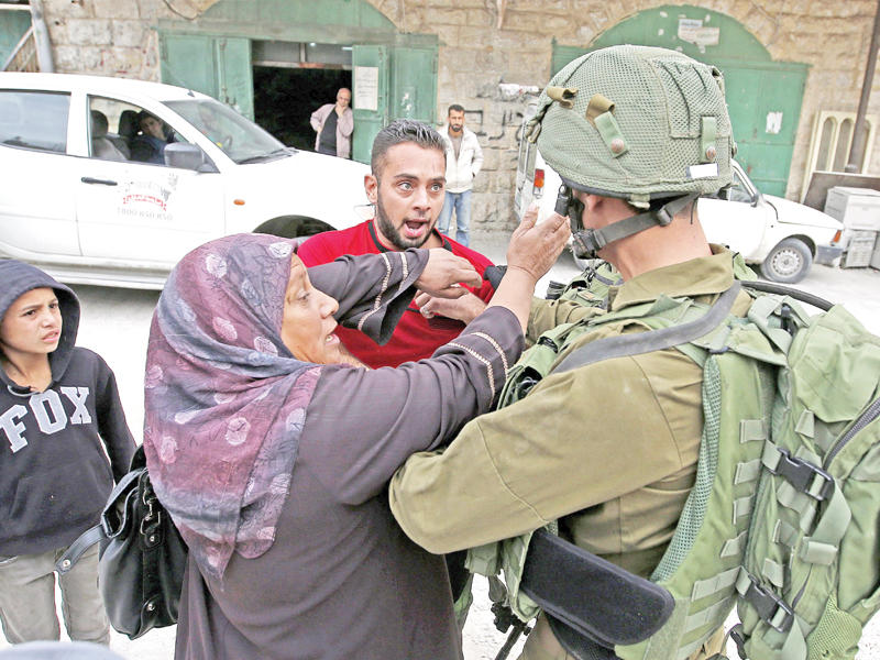 جندي إسرائيلي يواجه عائلة فلسطينية في الخليل أمس  (أي بي ايه)