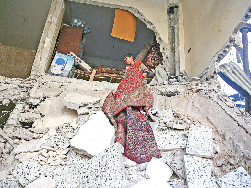 صبي يظفر بسجادة من منزله المدمر في غارة جوية على دوما أمس (رويترز)n