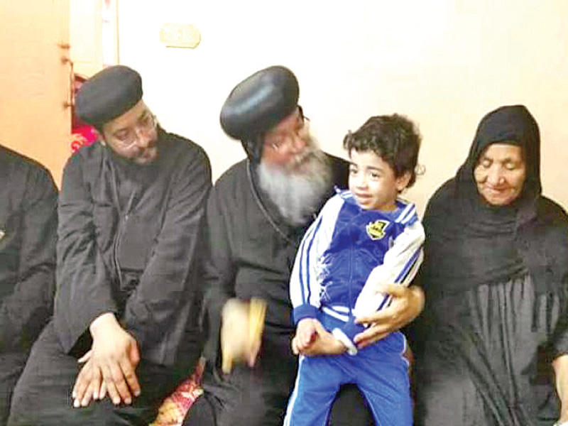 الانبا مكاريوس حاملا ابن القتيل خلال زيارة الى عائلته أمس الأول