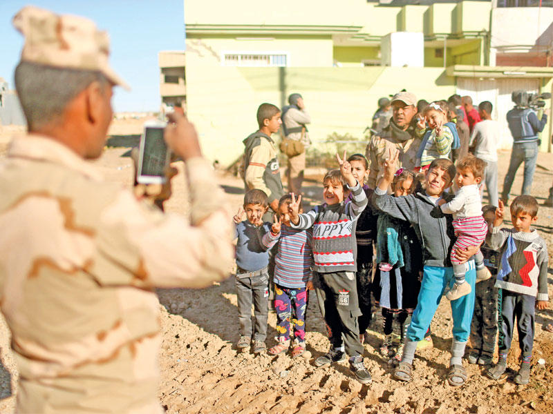 جندي عراقي يصور أطفالاً في ضاحية الشيماء جنوب شرق الموصل أمس (رويترز)