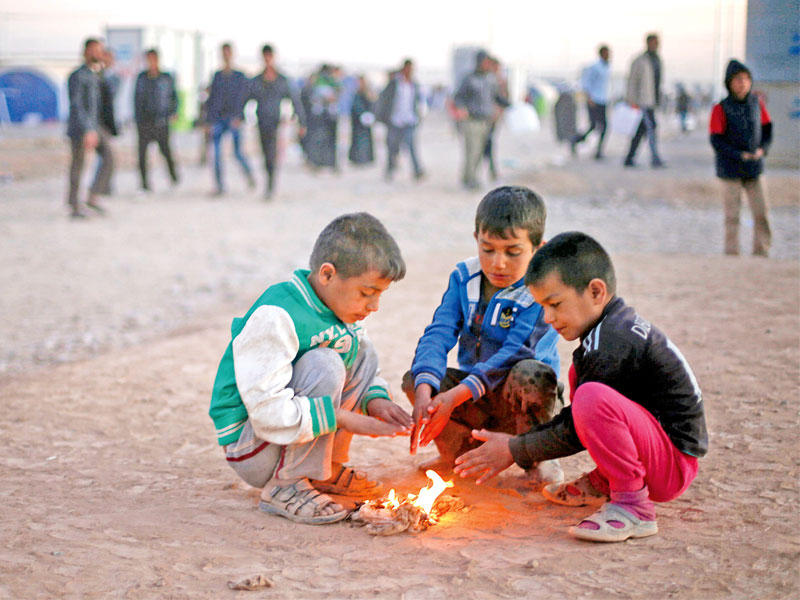 فتية عراقيون نازحون من الموصل يحاولون الحصول على قليل من الدفء مع اشتداد فصل الشتاء في مخيم الخازر أمس (رويترز)