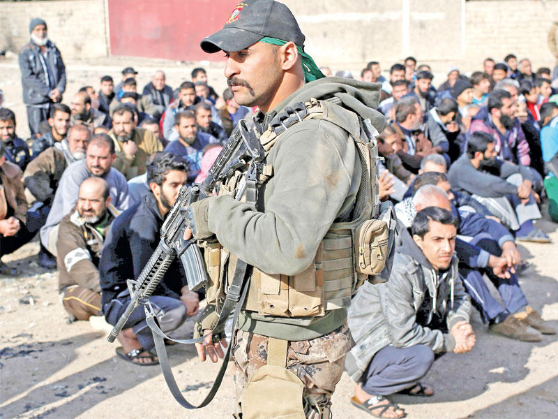 مسلح يحرس رجالاً اوقفوا بطريقة مذلة بانتظار اجراء تدقيق أمني في الموصل أمس  (رويترز)