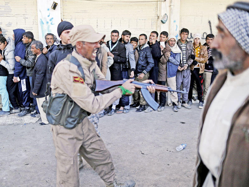 مقاتل موالٍ للحكومة يقوم بإذلال نازحين بينهم ذوو احتياجات خاصة ينتظرون دورهم للحصول على مساعدات بريطانية في حي قوقجلي شرق الموصل أمس (أ ف ب)