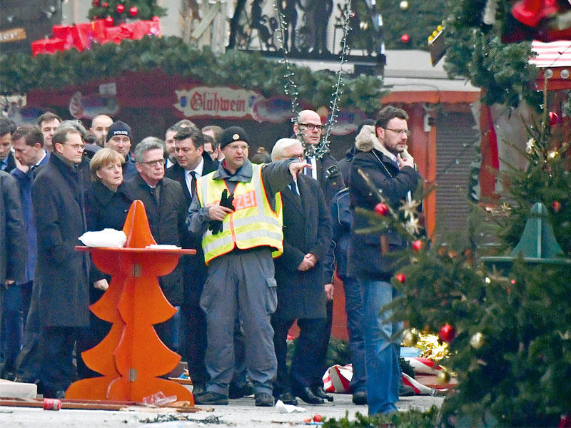 ميركل تستمع إلى شرح من رجل أمن في موقع الدهس وسط برلين أمسt(أ ف ب)