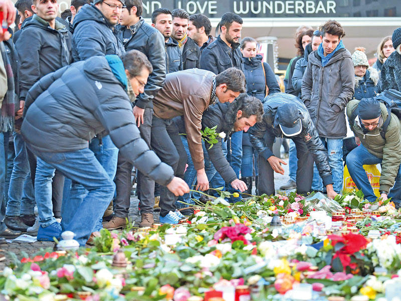 مجموعة من اللاجئين تضع الزهور في موقع الهجوم على سوق عيد الميلاد في برلين أمس(إيه بي إيه)n
