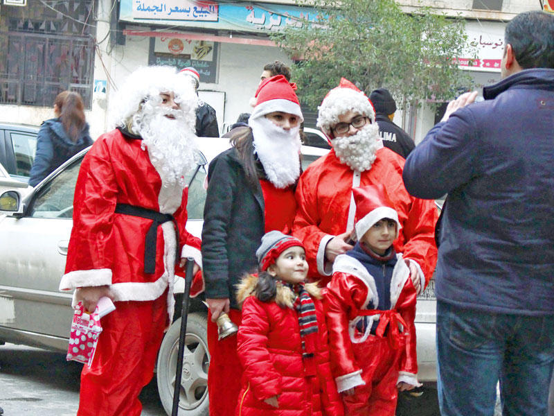 سوري يلتقط صورة لنجليه مع رجال يرتدون ملابس سانتا كلوز في حي العزيزية بحلب أمس الأول (أ ف ب)n