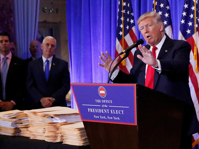 ترامب متحدثاً في مؤتمره الصحفي اليوم وإلى جانبه ولداه ومجموعة من عقود التخلي عن إدارة ممتلكاته لهما (رويترز)