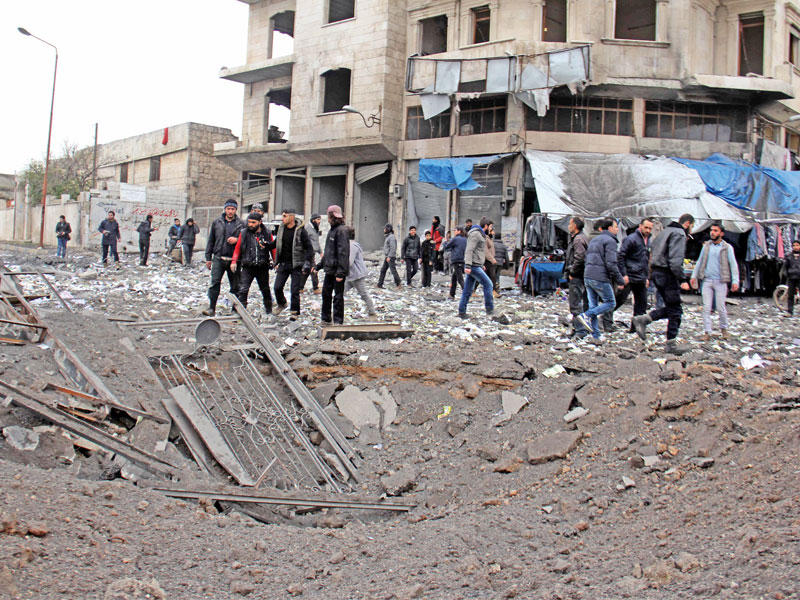 سوريون يتفقدون منطقة غارة جوية على محطة حافلات بإدلب أمسt(أ ف ب)