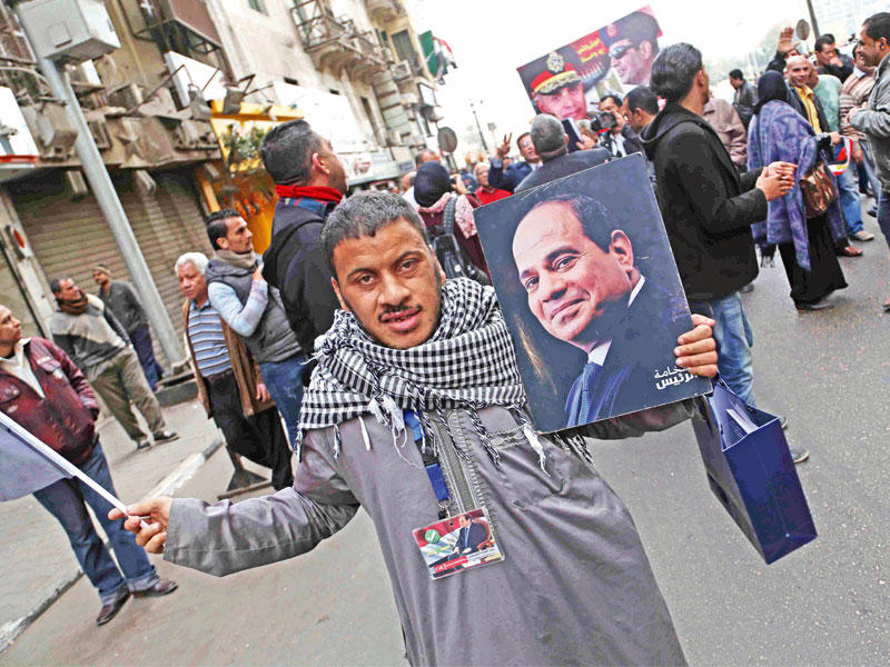 مصري يحمل صورة السيسي وهدية وزعتها عناصر «الداخلية» على المواطنين بمناسبة ذكرى الثورة قرب ميدان التحرير أمس (الجريدة)