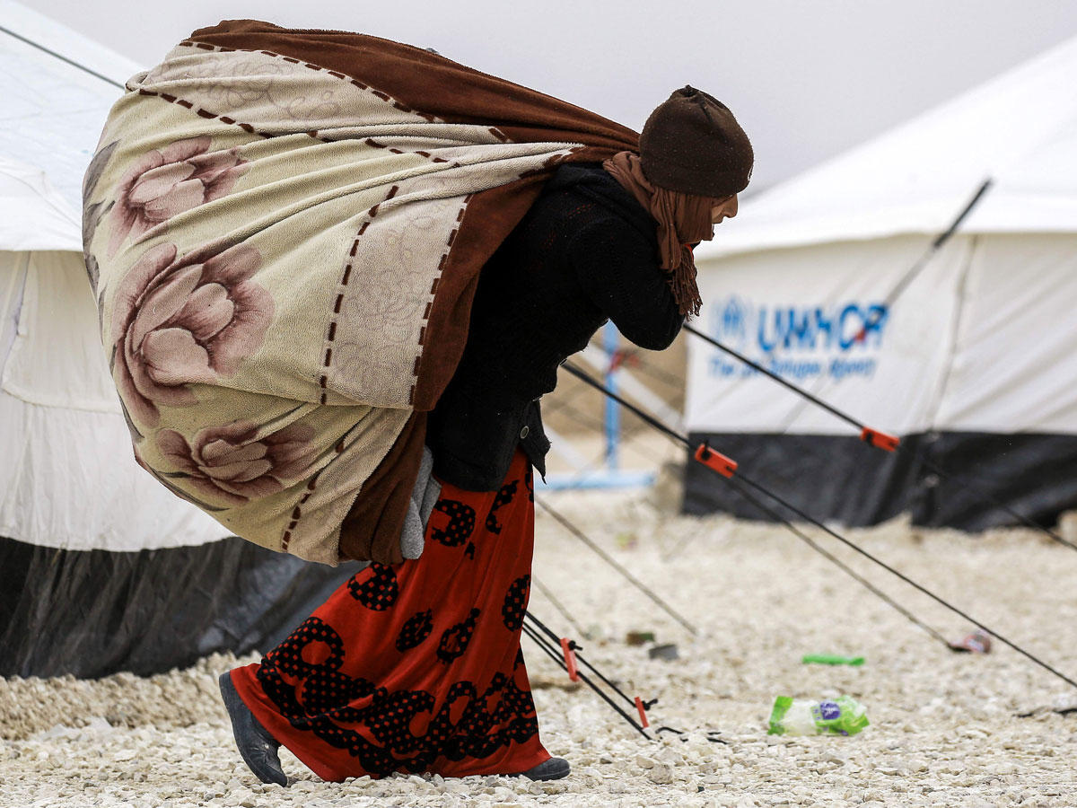 سورية نازحة من دير الزور تحمل متاعها وسط الثلوج في مخيم الأهوال بالحسكة أمس الأول	(أ ف ب)