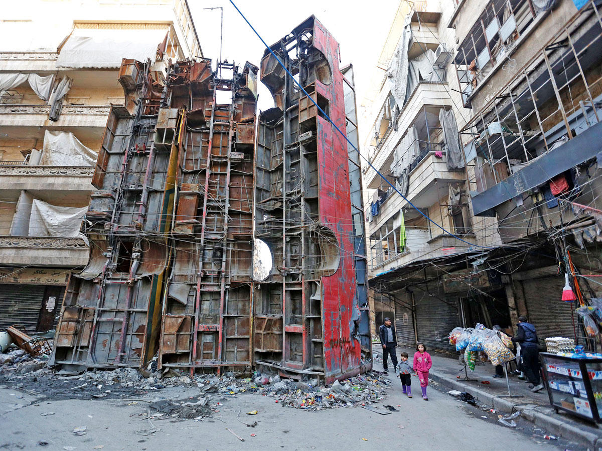 سوري يمر مع طفليه من نقطة تفتيش سابقة تغلقها حافلات مدمرة بحلب الشرقية أمس الأول (إي بي إيه)