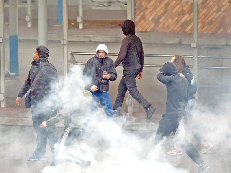 متظاهرون شباب يركلون القنابل الغازية التي ألقتها شرطة مكافحة الشغب أثناء مناوشات مع الشرطة شمال فرنسا أمس الأول ( أ ف ب)