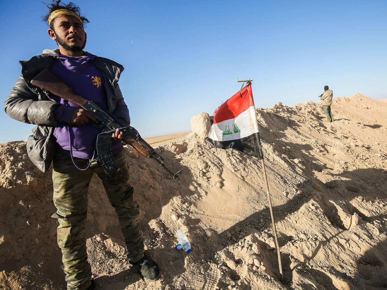 مقاتل من قوات الحشد الشعبي يحمل بندقية كلاشينكوف بجانب العلم العراقي في موقف دفاعي بالقرب من قرية في الخطوط الأمامية على مشارف تلعفر غرب الموصل.