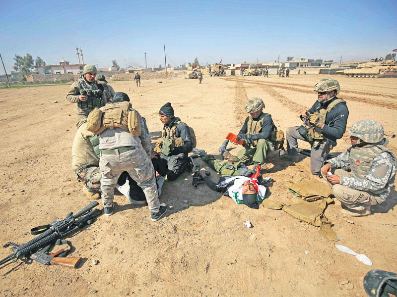 جنود عراقيون يعالجون أحد زملائهم خلال معارك الموصل أمس   (أ ف ب)