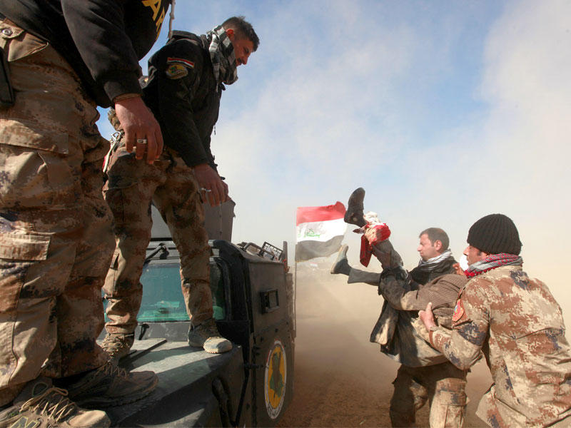 جنود عراقيون يساعدون جريحاً غرب الموصل أمس (رويترز)