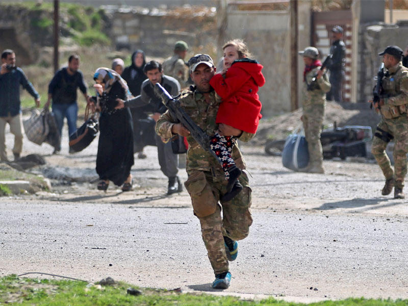 جندي القوات العراقية يحمل طفلة في حي الطيران الموصل