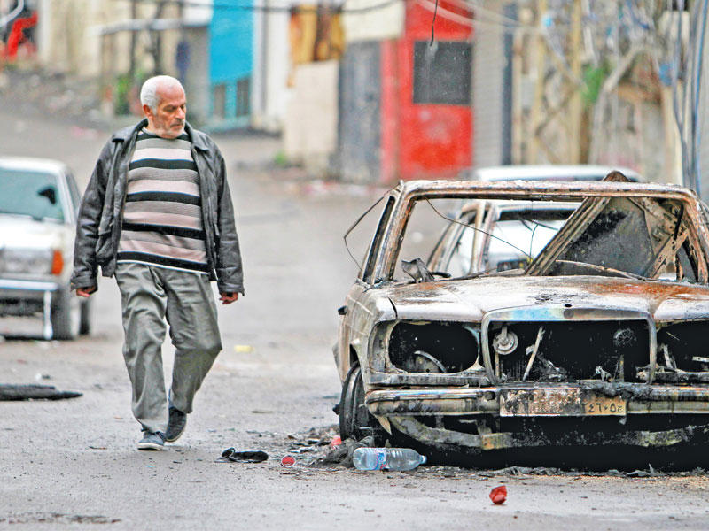 رجل يمشي بجانب سيارة بعين الحلوة بعد الاشتباكات أمس (رويترز)