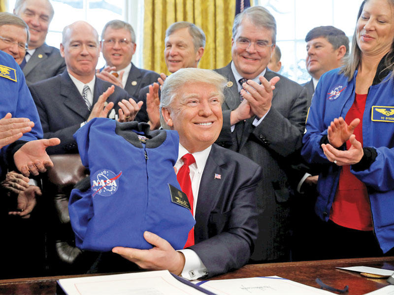 ترامب يتلقى سترة من وكالة الفضاء الأميركية «ناسا» بالمكتب البيضاوي في واشنطن  بمناسبة توقيعه قانوناً يسمح للوكالة بصرف 19.5 مليار دولار لمواصلة بعثتها لاستكشاف المريخ أمس (رويترز)