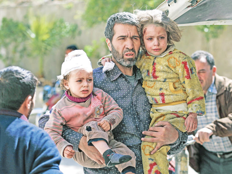 سوري يحمل طفلتيه بعد نجاتهما من غارة على مدينة حمورية في الغوطة  (أ ف ب)