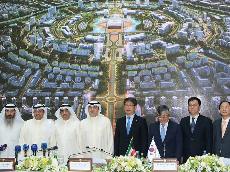 أبل ومسؤولو السكنية والجانب الكوري خلال توقيع العقد ويبدو في خلفية الصورة مخطط مدينة سعد العبداللهn