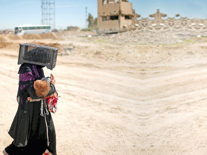 عراقية نازحة من الموصل باتجاه حمام العليل تضع على رأسها صندوقاً لحماية ابنها من الشمس أمسn (رويترز)