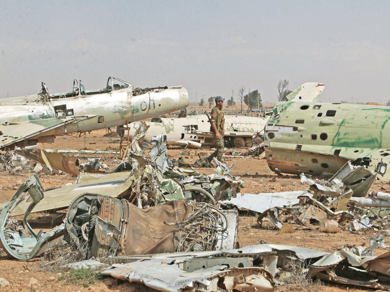 مقاتل من «قسد» بين حطام الطائرات الحربية في مطار الطبقة العسكري قرب الرقة أمس  (رويترز)
