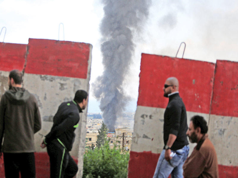 لبنانيان يشاهدان الاشتباكات في مخيم عين الحلوة من وراء حاجز اسمنتي أمس (رويترز)