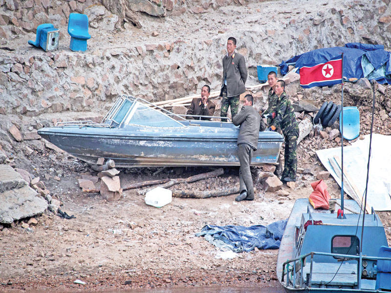 جنود كوريون شماليون بجوار زوارق قديمة على طول نهر يالو بالقرب من سينويغو مقابل مدينة داندونغ الحدودية الصينية أمس (أ ف ب)